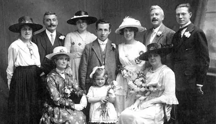 Old photograph of a wedding party: the bride with her bouquet, the groom, family and a small bridesmaid