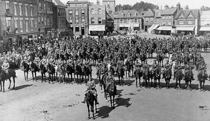 Old photograph of mounted troops drawn up in rows in a town square lined with shops